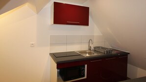 Une cuisine compacte équipée d’un four à micro-ondes encastré, d’un évier et d’un meuble rouge placé au-dessus du plan de travail.