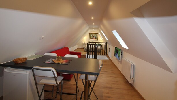 Une pièce compacte et bien éclairée, comprenant une table à manger, des chaises, un canapé rouge et une petite cuisine.