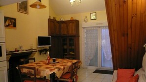 A dining area with a table and chairs, a television, wooden cabinets, and a sliding glass door leading to a balcony. - Small corner for sinners and hikers, calm relaxation in the country. (Saint-Épain)