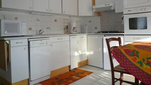A kitchen with white cabinets, a microwave, a coffee maker, and a table with a fruit-patterned tablecloth. - Small corner for sinners and hikers, calm relaxation in the country. (Saint-Épain)