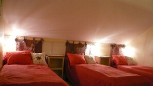 A room with two single beds, each with a red bedspread and pillows, a small wooden nightstand, and a wall-mounted shelf. - Small corner for sinners and hikers, calm relaxation in the country. (Saint-Épain)