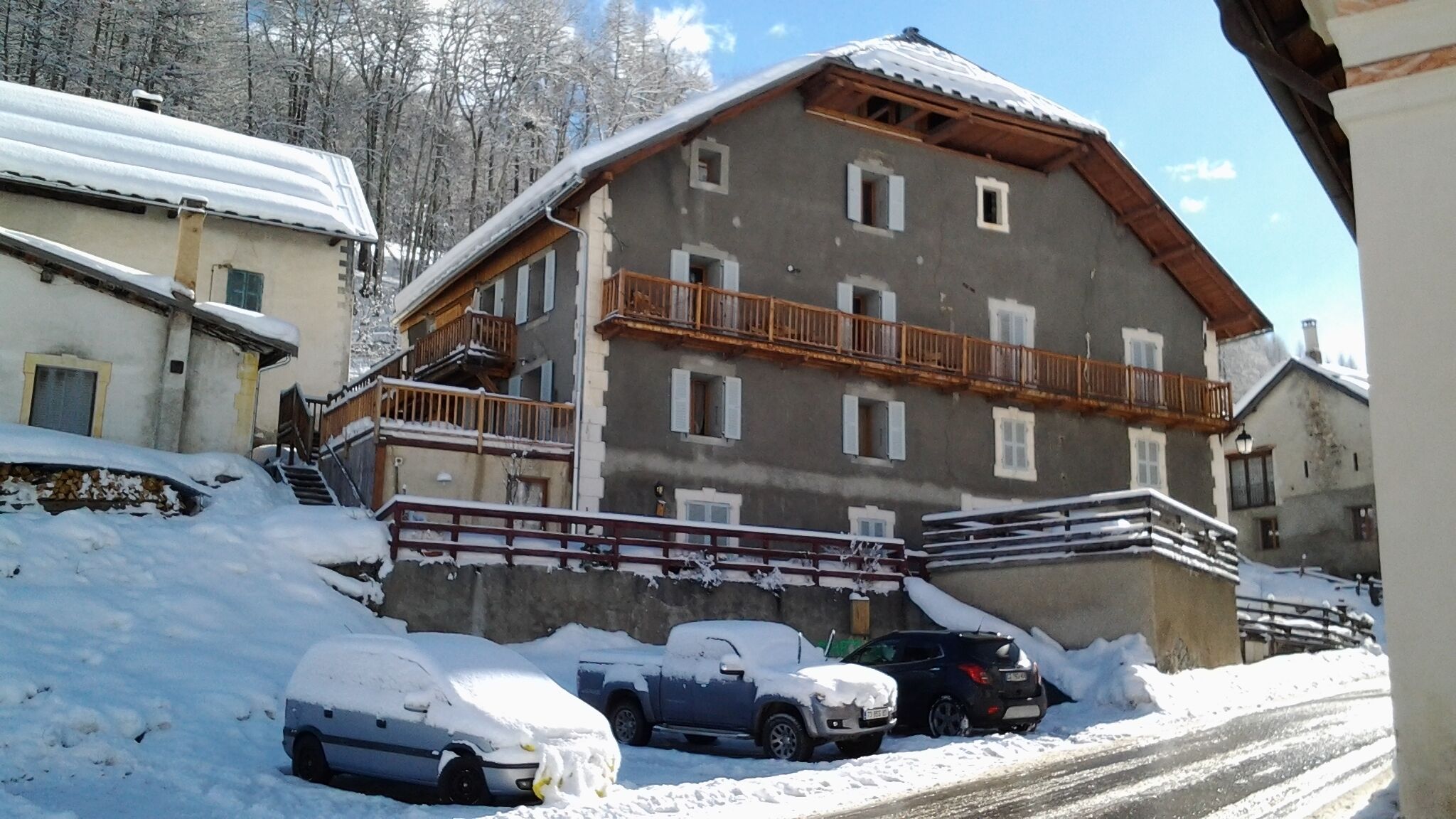 A multi-story building with a balcony, surrounded by snow-covered ground and parked cars.