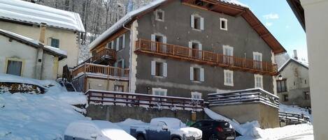 A multi-story building with a balcony, surrounded by snow-covered ground and parked cars.