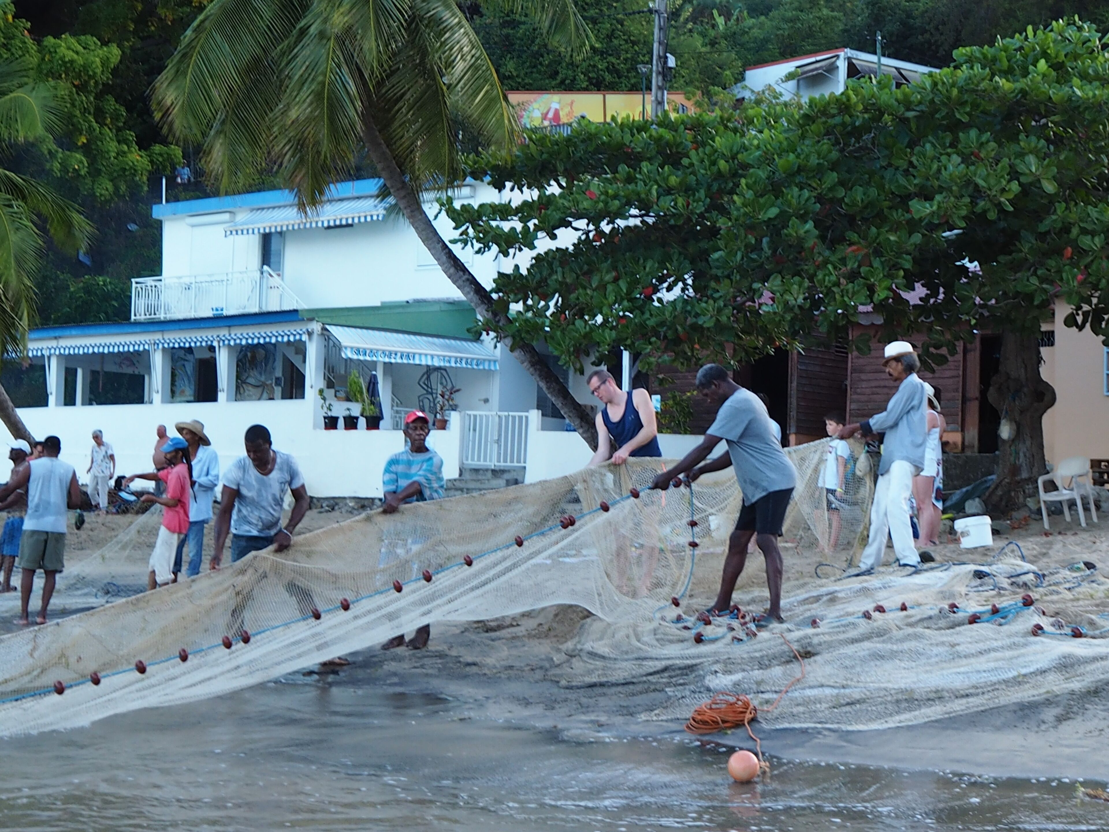 A beach scene with people fishing and a building in the background.