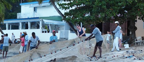 A beach scene with people fishing and a building in the background.