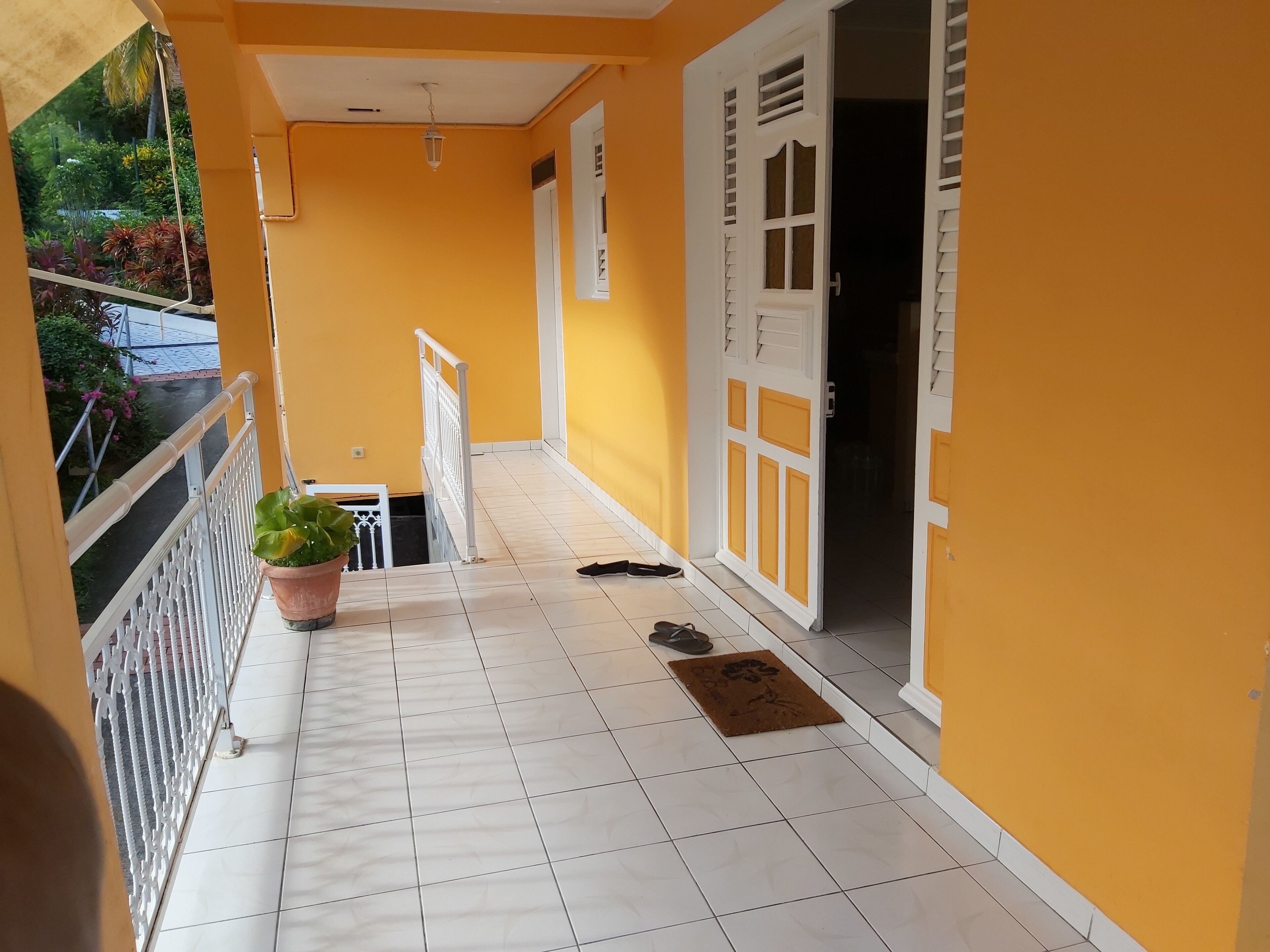 A corridor with white tiled flooring, a potted plant, and a pair of shoes on a mat.