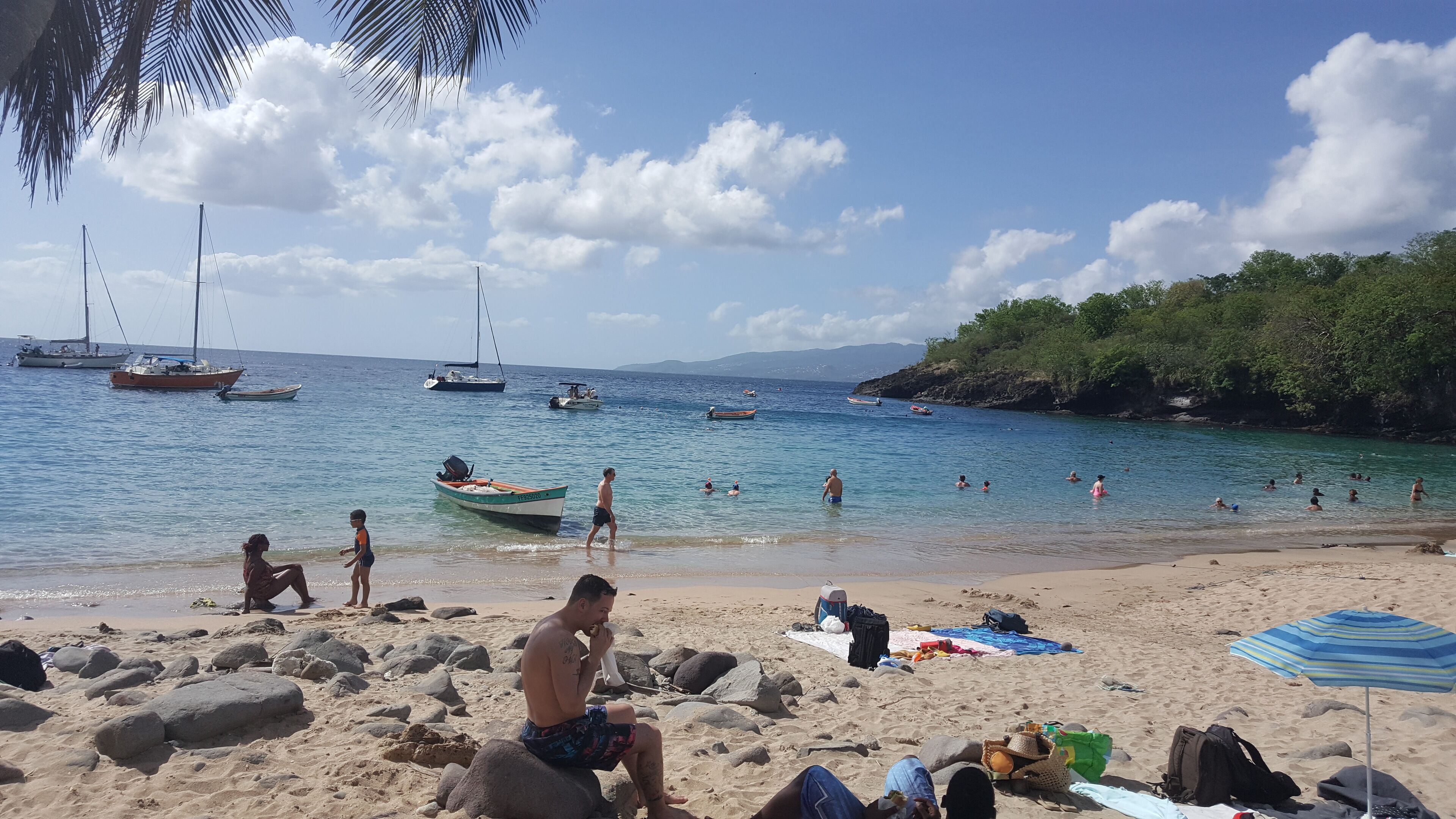 A beach with people swimming and boats in the water.