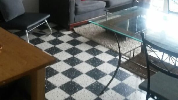 En stue med et ternet gulv, en grå sofa med røde puder, en rød pendel og et billede på væggen.