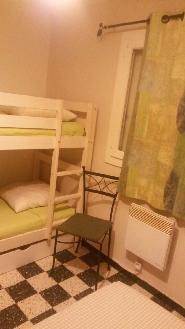 A bunk bed room with a checkered floor, a radiator, and a window with a curtain.