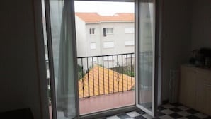 Et værelse med et skakternet gulv, en skydedør til en balkon med gelænder i metal og et lille skab til højre.