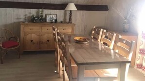 Ein Essbereich mit Holztisch und Stühlen, einem Schrank mit Schubladen, einer Lampe und einer Vase mit Trockenpflanzen.