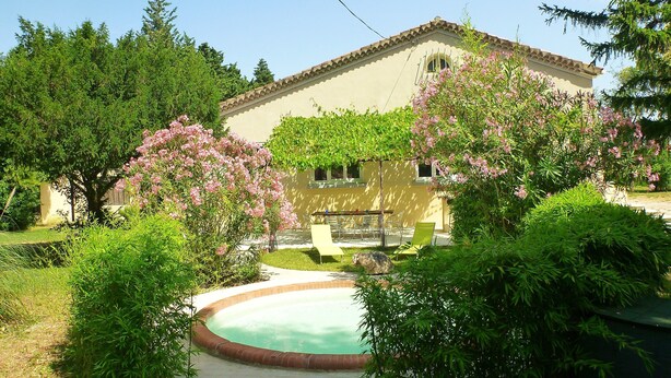 Une maison avec une piscine, entourée d’une végétation luxuriante et d’arbres en fleurs.