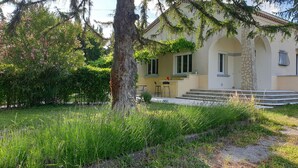 Une maison avec un pilier en pierre, un petit porche et un jardin où poussent différentes espèces de plantes.