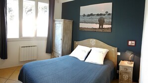 Een slaapkamer met een bed, een nachtkastje, een radiator, een raam en een foto aan de muur.