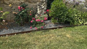 A stone wall with a statue, surrounded by a garden with various flowers and plants. - Charming house completely renovated with swimming pool in the heart of the village for 4 people (Capestang)