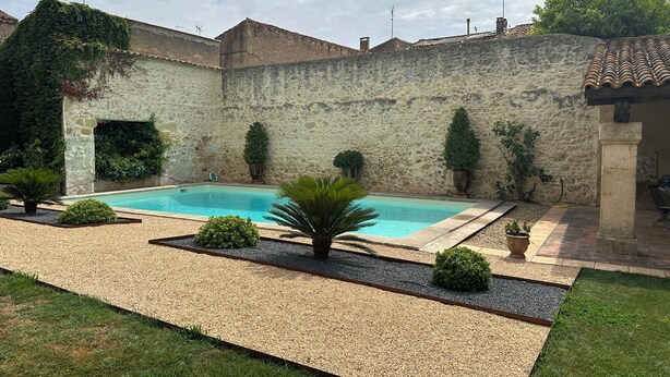 A swimming pool surrounded by a stone wall, with a small garden area and a grassy lawn. - Charming house completely renovated with swimming pool in the heart of the village for 4 people (Capestang)