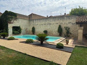 Une piscine entourée d’un mur de pierre, avec un petit jardin et une pelouse.