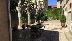 An outdoor patio with a table and chairs, surrounded by potted plants and trees. - Charming house completely renovated with swimming pool in the heart of the village for 4 people (Capestang)