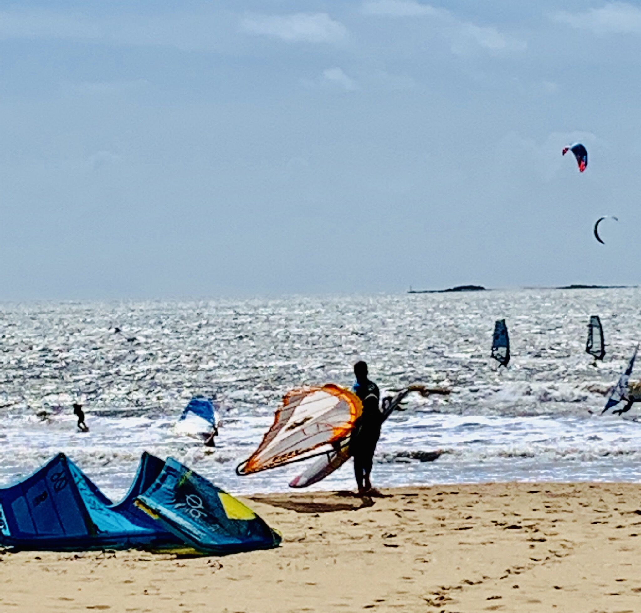 Een strand met mensen die windsurfen en iemand die een grote kite draagt.