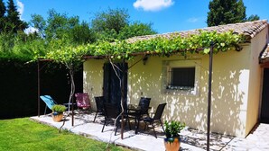 A covered patio with outdoor furniture, a pergola with climbing plants, and a small window.