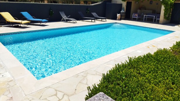 A rectangular swimming pool with clear blue water, surrounded by a stone deck. There are lounge chairs along the poolside, and a small statue is visible near the edge.