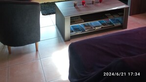 A living room with a sofa, a coffee table with magazines, a television, and red curtains.