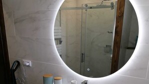 Une salle de bain avec un miroir rond, un lavabo blanc et deux tiroirs.
