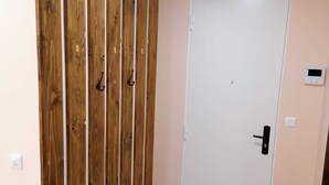Un couloir avec un mur recouvert de panneaux de bois, une porte blanche et un thermostat fixé au mur.