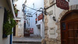 A narrow street with a pizzeria sign, a staircase leading to a building, and a wooden door.