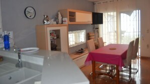 A kitchen with a sink, a dining table with chairs, and a television on a shelf.