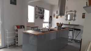A modern kitchen with a central island, stainless steel appliances, and a hanging pot rack. - Entire home Les Mille Roses (Nieul-sur-Mer)