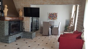 A living room with a fireplace, a flat-screen TV, a colorful abstract painting, and a red sofa. - Entire home Les Mille Roses (Nieul-sur-Mer)