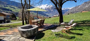 A patio with a table and chairs, a stone fire pit, and a view of snow-capped mountains.