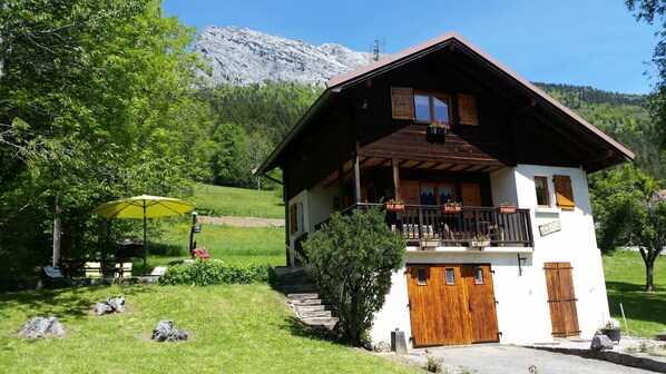 A chalet with a balcony, wooden doors, and a mountain backdrop.