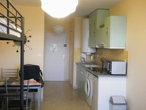 Compact kitchen with a washing machine, microwave, and sink, featuring a single cabinet and a small trash bin.