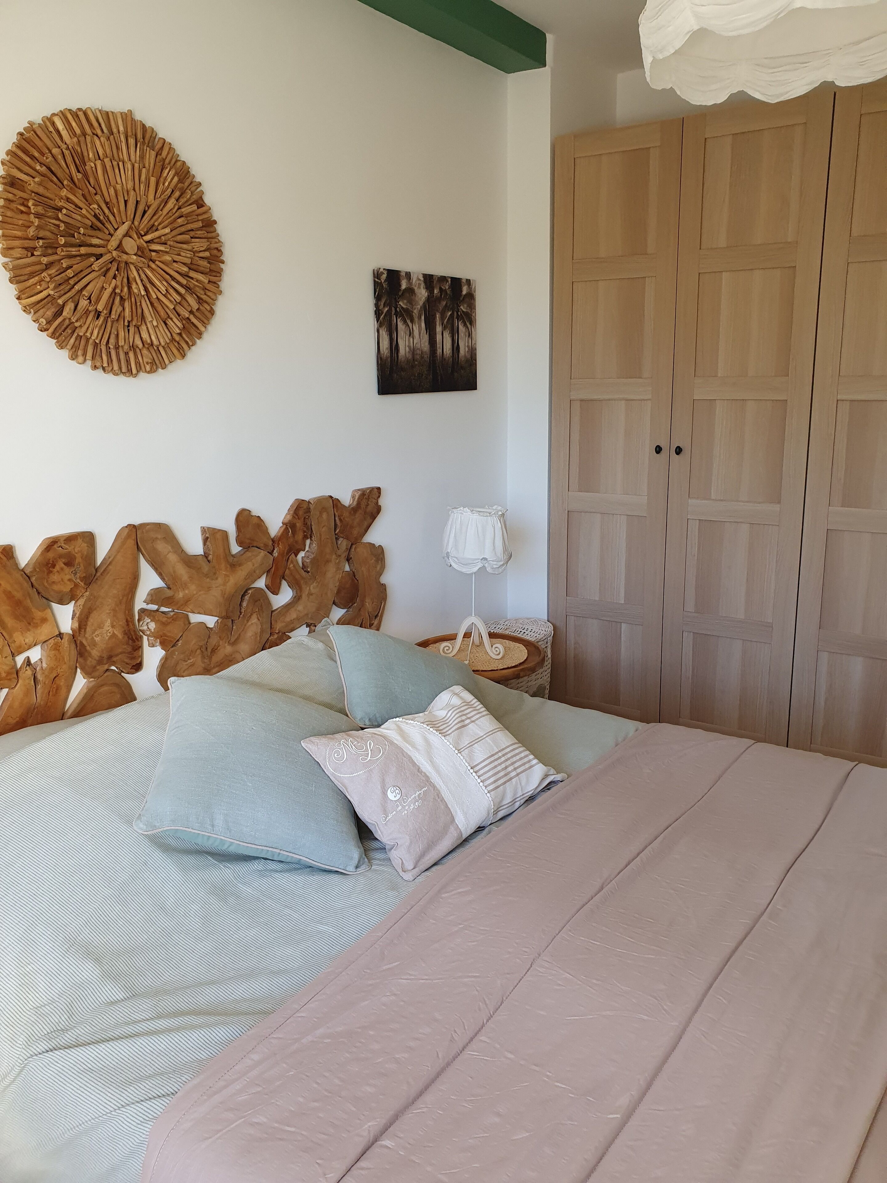Une chambre à coucher comprenant un lit, une tête de lit en bois, une œuvre d’art murale, une armoire et une table de chevet avec une lampe.