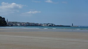 Una playa con un pueblo al fondo, incluyendo una torre destacada.