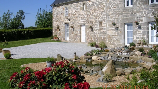 Una casa de piedra con un camino pavimentado, un pequeño estanque y plantas en flor.
