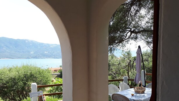 A deck with a table and chairs overlooking a lake and mountains.