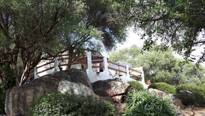 A white building with a wooden bridge, surrounded by large rocks and greenery.