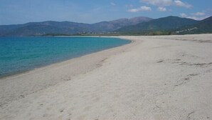 A beach with clear turquoise water, a sandy shore, and mountains in the background.