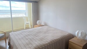 Un dormitorio con cama, mesitas de noche, una silla y vista al océano.