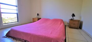 A bedroom with a bed, two nightstands, a window, and a view of the outside. - Appt "Longanis" St-Gilles Les Bains - T3 pleasant and quiet sea view - 4 pers (Saint-Gilles les Bains)