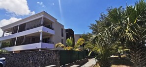 A modern two-story house with a balcony, surrounded by a stone wall and palm trees. - Appt "Longanis" St-Gilles Les Bains - T3 pleasant and quiet sea view - 4 pers (Saint-Gilles les Bains)