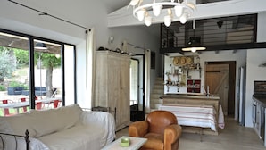 A spacious living area with a sofa, armchairs, a small table, and a kitchen in the background.