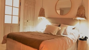 A bedroom with a large bed, a round mirror above it, and two hanging lamps.