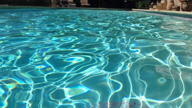 A clear swimming pool with visible water patterns, lounge chairs, umbrellas, and a stone wall with potted plants. - Large salted swimming pool heated from May to September for 4 people (Vence)