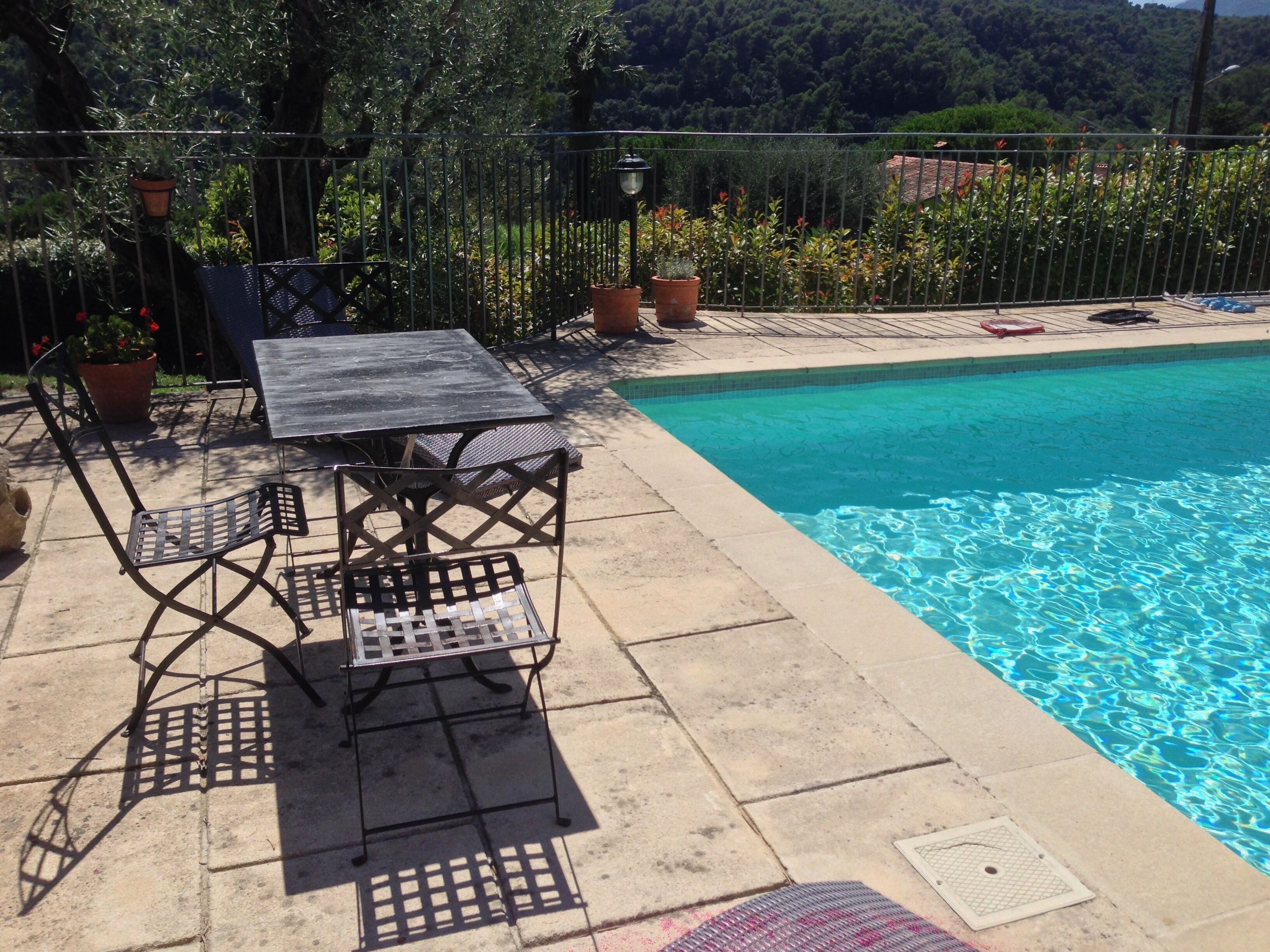 A poolside area with a metal table and chairs, a tiled deck, and a pool.