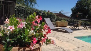 A poolside area with lounge chairs, a table, and a potted plant with flowers. - Large salted swimming pool heated from May to September for 4 people (Vence)