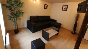 Ein Wohnzimmer mit einer schwarzen Couch, einem Couchtisch, einem Blumentopf und Holzboden.